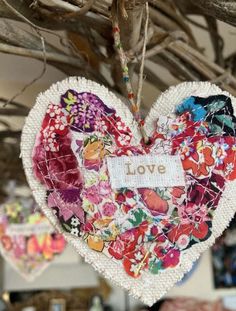 two heart shaped ornaments hanging from a branch with the word love written on it and flowers all over them