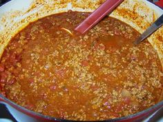 a red pot filled with chili and bread on top of a stove next to a spatula