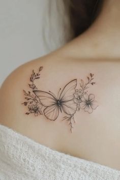 a woman's shoulder with a butterfly and flowers tattoo on the back of her shoulder