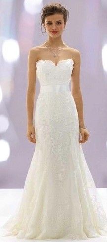 a woman in a white wedding dress standing on a runway with her hands behind her back