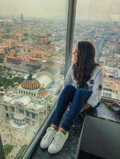 a woman sitting on top of a tall building looking out at the city from a high rise