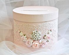 a white hat box with pink flowers and pearls on the top, sitting on a veiled surface