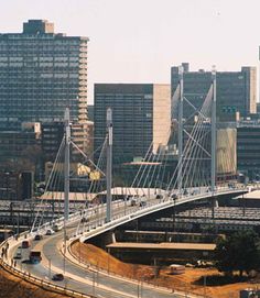 a bridge over a road with cars driving on it and tall buildings in the background