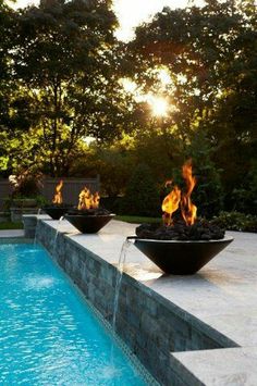 two black bowls sitting on top of a swimming pool next to a fire pit with flames in it