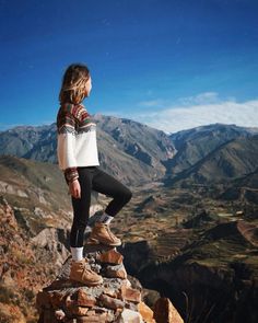 a young woman standing on top of a rock formation with mountains in the back ground