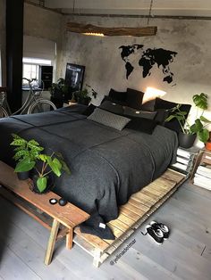 a bed with black sheets and pillows in a room filled with potted plants next to a wooden bench