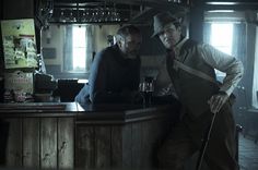 two men standing at a bar in an old - fashioned pub, one holding a cane