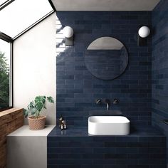 a bathroom with blue tiles and a round mirror above the sink, along with a potted plant