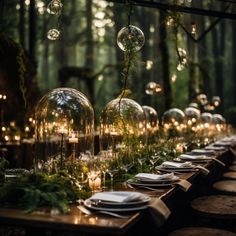 a long table is set with candles, plates and glass globes in the forest