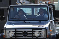 two people sitting in the driver's seat of a mercedes benz truck on a city street