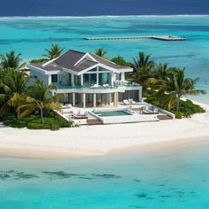 an aerial view of a large white house with palm trees in the foreground and clear blue water behind it