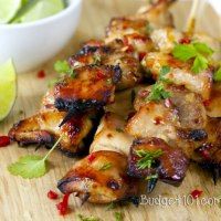 chicken skewers on a wooden cutting board with limes and cilantro