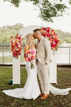 a bride and groom kissing in front of an arch decorated with colorful flowers at their wedding