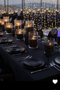 a table set with black plates and silverware is lit by candles in front of a cityscape