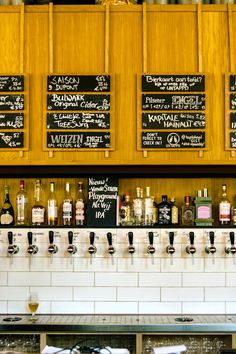 there are many different types of alcohol on the shelves in this restaurant bar that is lined with chalkboard menus