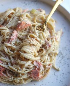 a white plate topped with pasta covered in sauce and meat next to a gold fork