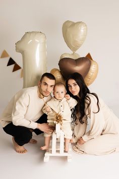 a man and woman holding a baby in front of balloons