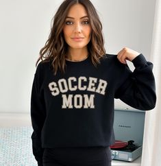 Are you the ultimate Soccer Mom, cheering on your superstar player from the sidelines? Celebrate your devotion to the beautiful game with our custom "Soccer Mom" sweatshirt, where style meets soccer spirit! This cozy and fashionable sweatshirt is perfect for chilly match days or casual outings, and it's personalized just for you. 🌟 Key Features 🌟 ✨ "Soccer Mom" Front Design: Let everyone know you're the proudest soccer mom with our eye-catching "Soccer Mom" text on the front. It's more than ju Crew Neck Top With Team Logo For Cheerleading, Black Football Season Sweatshirt, Black Team Spirit Sweatshirt With Relaxed Fit, Relaxed Fit Tops With Team Name For Football Season, Black School Spirit Sweatshirt For Sports, Collegiate Black Sweatshirt For Football Season, Customizable Tops For Sports Season Fan Merchandise, Black Sports Fan Sweatshirt For Sports Season, Black Varsity Sweatshirt With Team Name