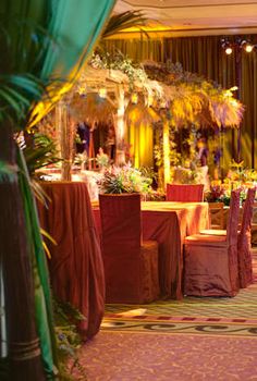 a banquet hall with tables and chairs covered in cloths, decorated with palm trees