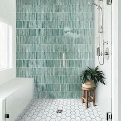 a green tiled shower with a plant in the corner and a stool next to it