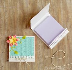 an open box with a flower on it next to a small notepad and string