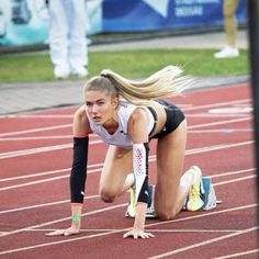 a woman kneeling down on top of a track next to a red and white field