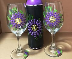 three wine glasses with painted flowers on them next to a purple bottle and corkscrew