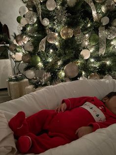 a baby is sleeping on a white bed in front of a christmas tree with lights