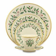 a white and gold christmas dinnerware set with holly designs on it, including two cups and saucers