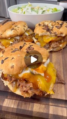 three cheeseburgers on a cutting board with a bowl of salad in the background