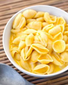 a white bowl filled with macaroni and cheese on top of a bamboo mat