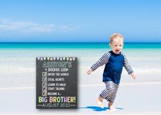 a little boy running on the beach with a big brother sign in front of him