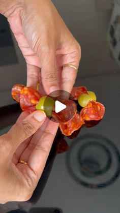 two hands are holding an object in the shape of a flower with olives on it