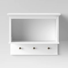 a white shelf with three drawers and two knobs on the bottom, against a gray wall