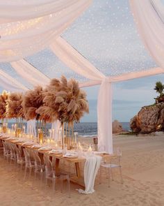 a long table set up on the beach with candles and pamolite centerpieces