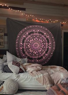 a bed covered in blankets and pillows next to a wall with a tapestry on it