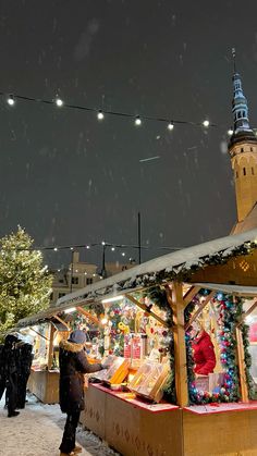 people are standing outside in the snow near a christmas market with lights and decorations on it