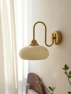 a wall light that is on the side of a wall next to a chair and potted plant