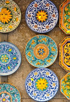 many colorful plates with designs on them are arranged in rows against a stone wall and floor