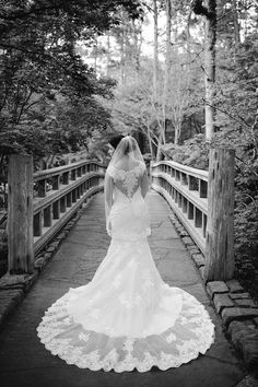 a woman in a wedding dress standing on a bridge looking at the trees and bushes