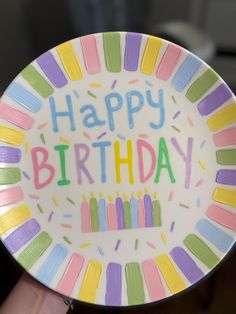 a hand holding a happy birthday plate with candles on it