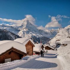 snow covered mountains and houses in the foreground with people walking on the sidewalk below