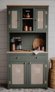 a green hutch with wicker doors and baskets on the floor next to it