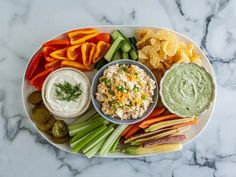 a platter with dips, chips and vegetables on it sitting on a marble table