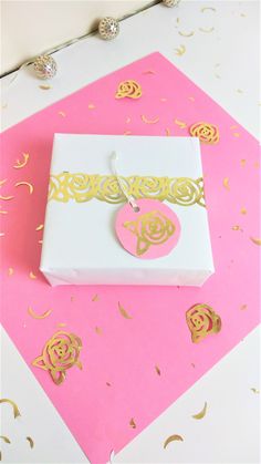 a pink and white box with a gold monogrammed tag sitting on top of it