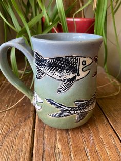 a coffee cup with fish on it sitting next to a potted plant