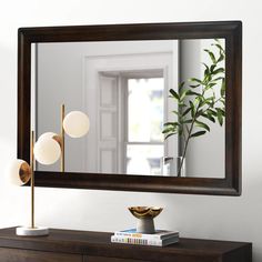 a mirror sitting on top of a wooden dresser next to a vase and book shelf