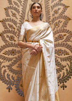 a woman in a white and gold sari standing next to a wall with an intricate design