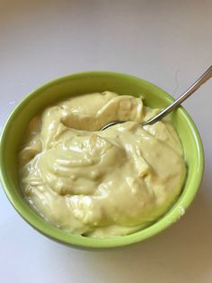 a green bowl filled with cream sitting on top of a white table next to a spoon