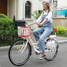 a woman in overalls riding a bicycle with a basket on the front and side